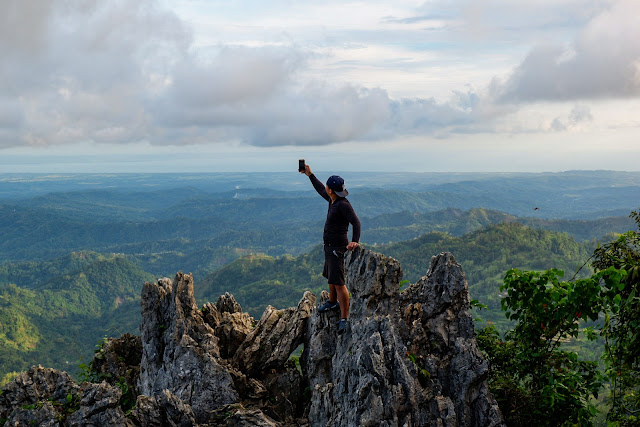 a man standing on top of rocky formation holding a phone